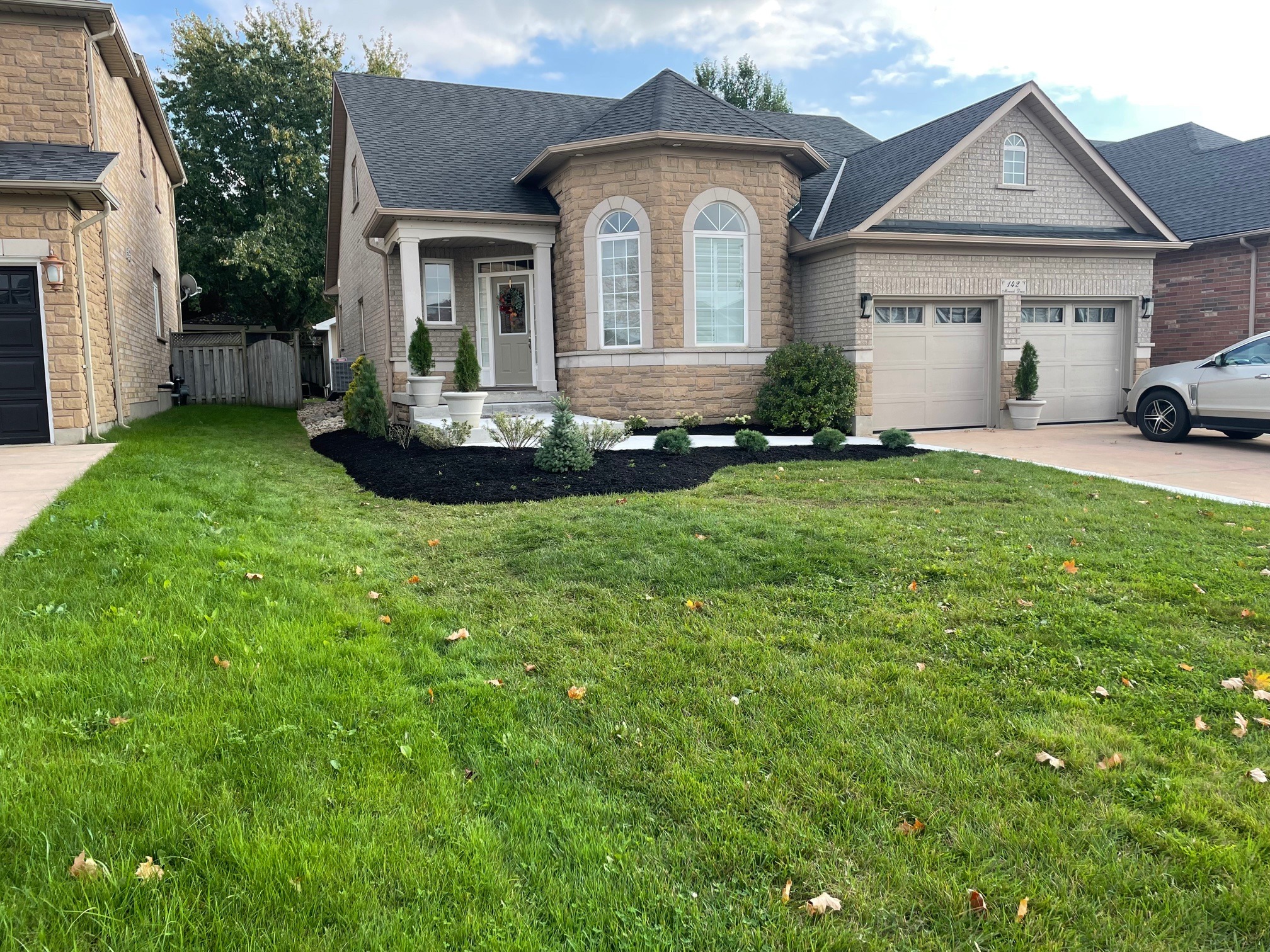 A suburban house with a well-maintained lawn, two-car garage, white-trimmed windows, and stone facade, flanked by adjoining residences under a blue sky.