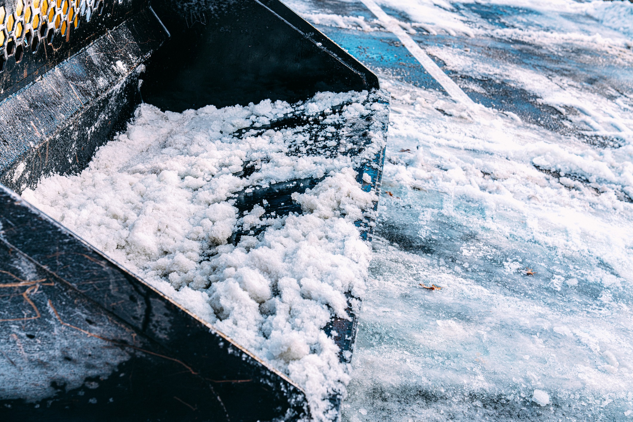 A snowplow collects snow from an icy, snowy parking lot, clearing paths and ensuring safe parking for vehicles.